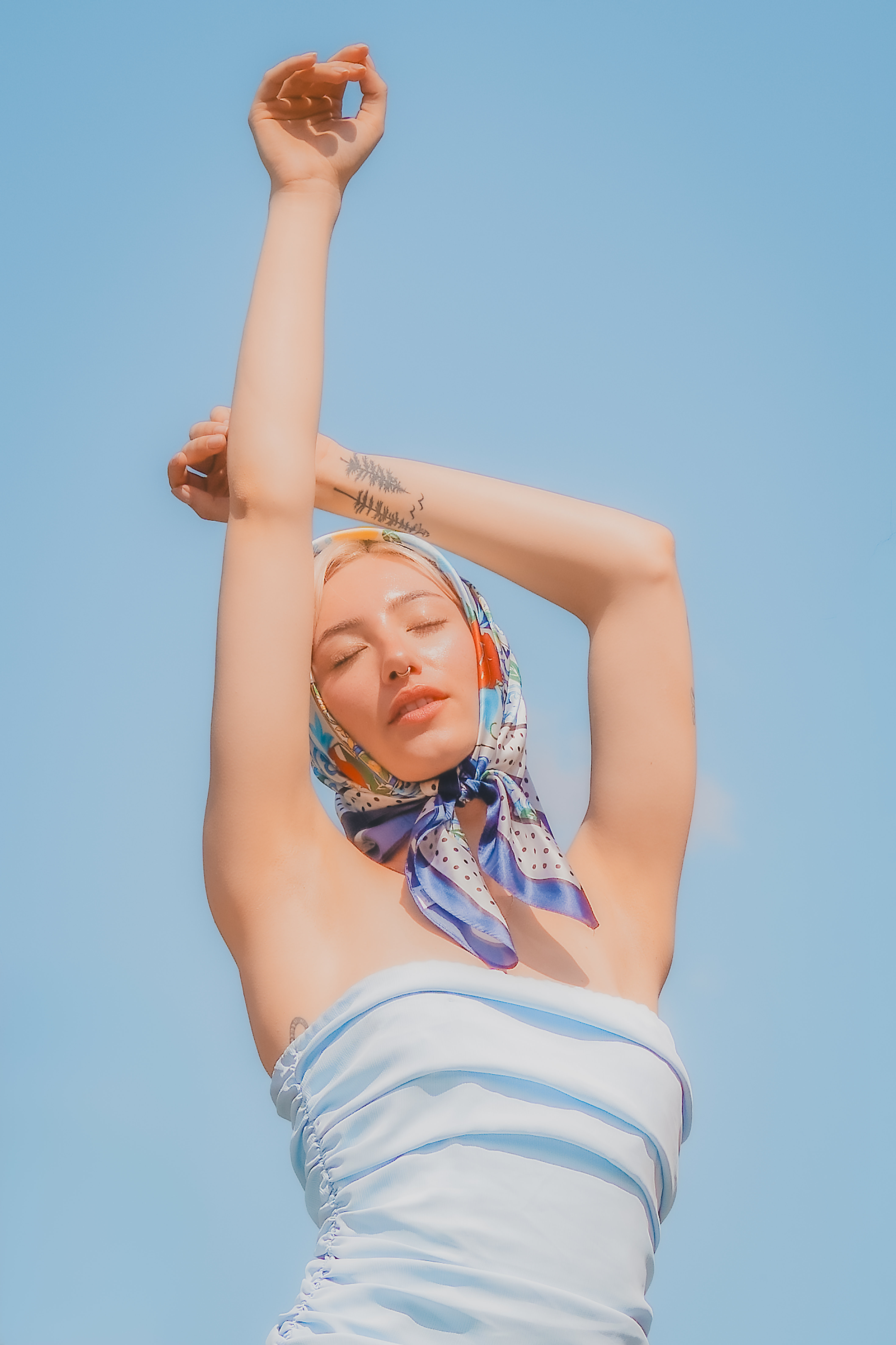 Modelo con pañoleta estampada y los brazos en alto sobre fondo azul claro