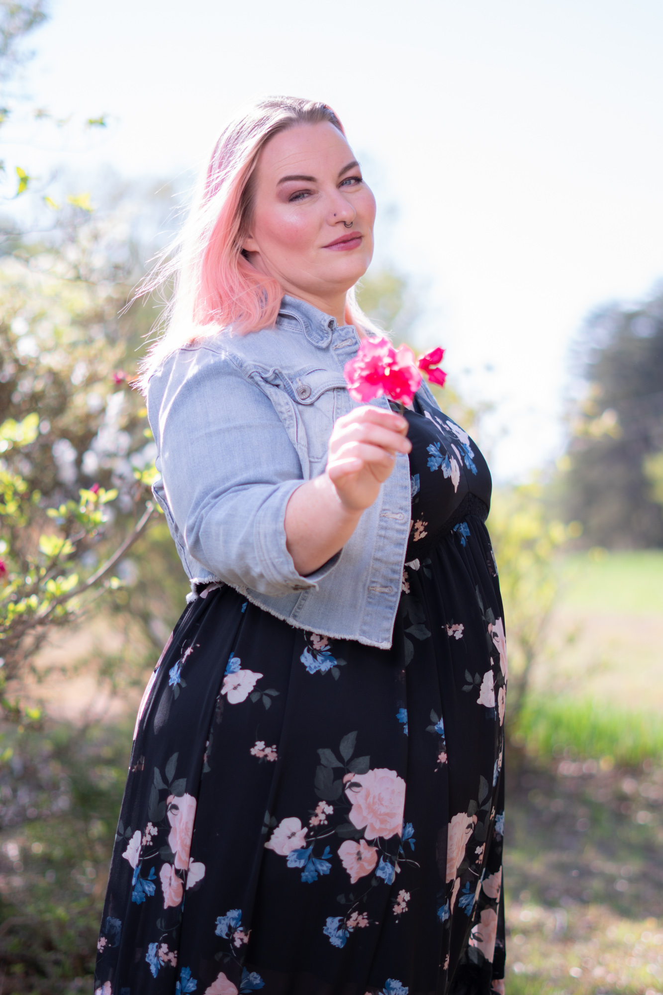 Mujer con chaqueta floreada sosteniendo una flor rosa en un jardín