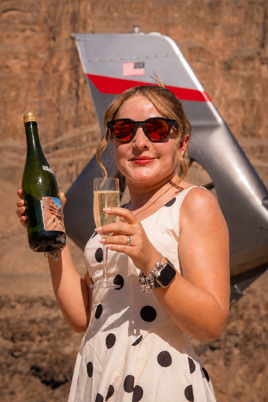 Mujer con gafas de sol sosteniendo una botella y una copa de champaña frente a una avioneta en el Gran Cañón