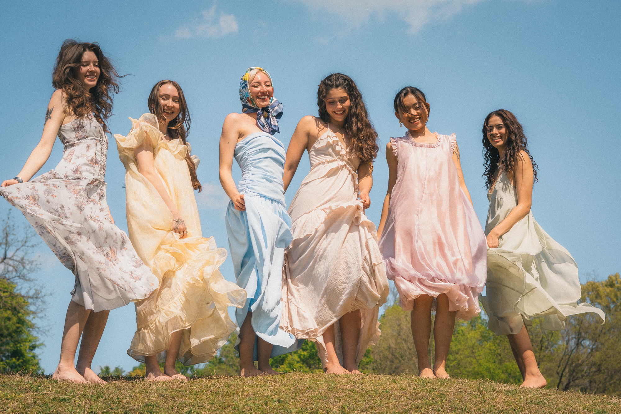 Grupo de mujeres con vestidos vaporosos caminando por un prado