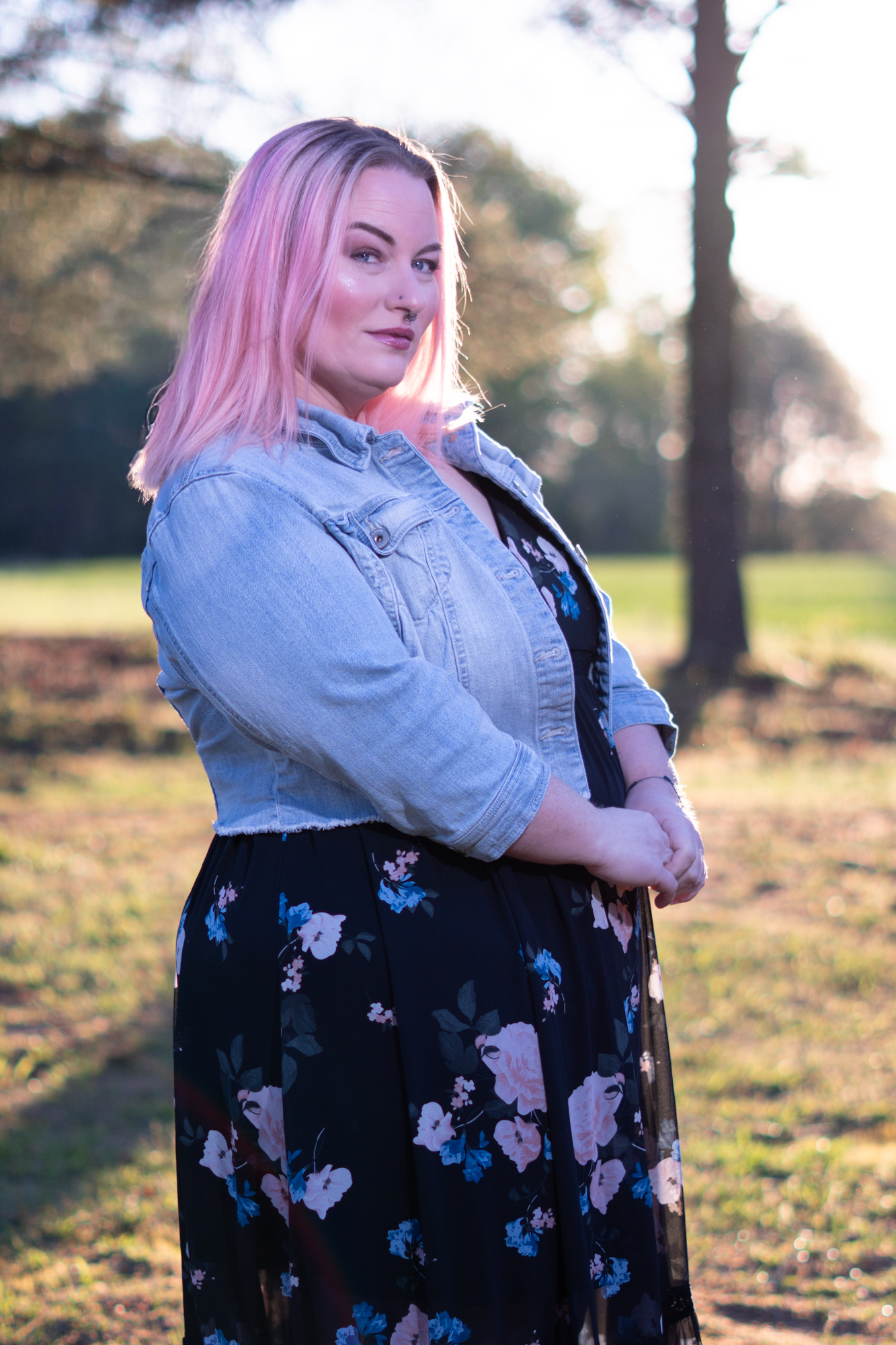 Mujer de cabello rosa con blusa floreada y chaqueta de jean en un jardín